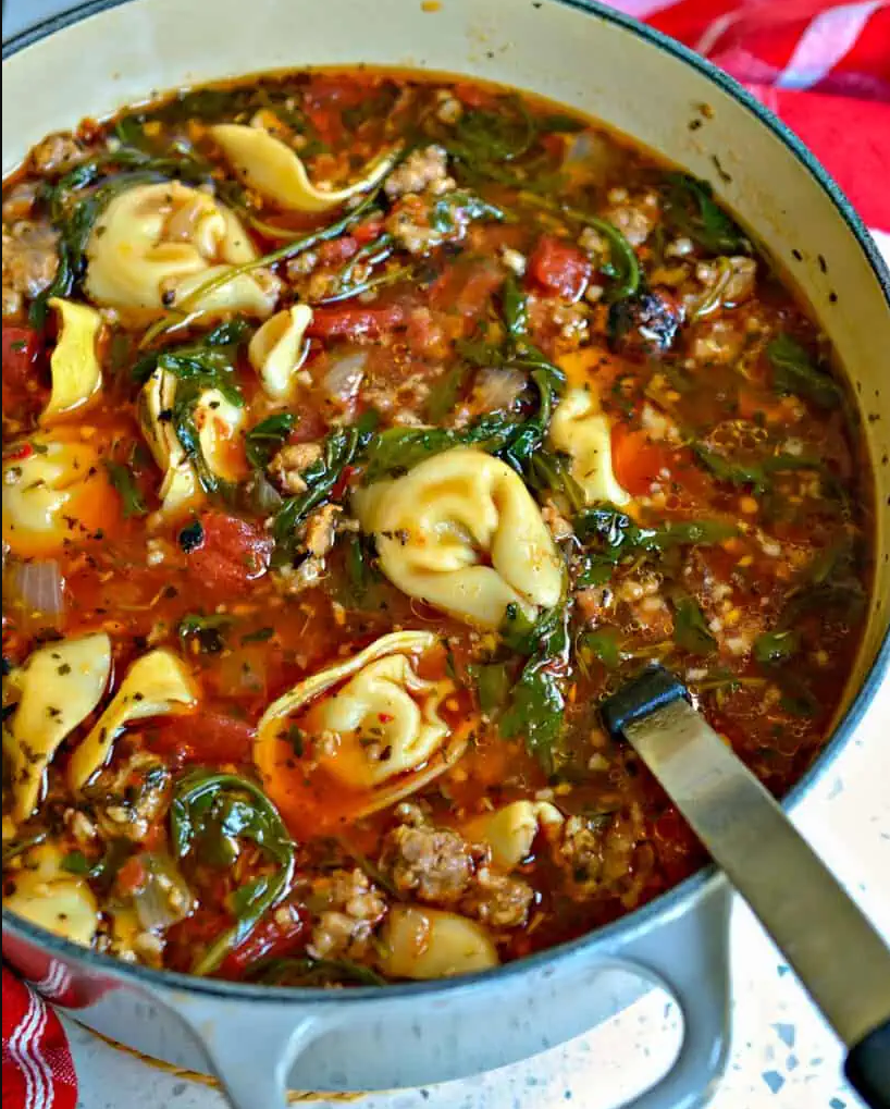 Italian Sausage Tortellini Soup: A hearty bowl filled with sausage, tomatoes, tortellini, and arugula, garnished with Parmesan cheese and fresh thyme.