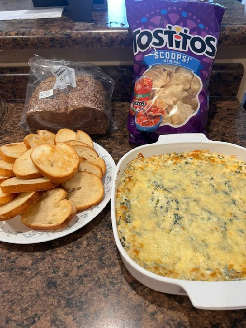 Spinach Artichoke Dip - A tempting bowl of creamy dip with melted cheese on top, served with sliced French bread.