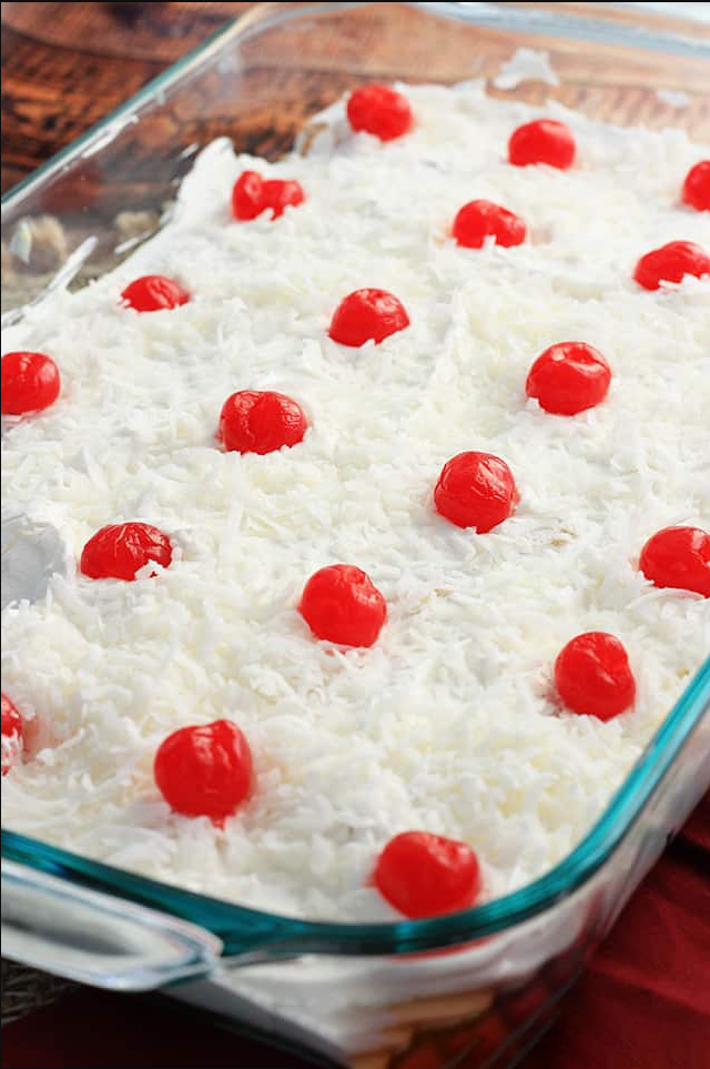 Italian No Bake Cake presented on a plate, showcasing the layers of Vanilla Wafers, pineapples, coconut, and cherries, topped with Cool Whip.