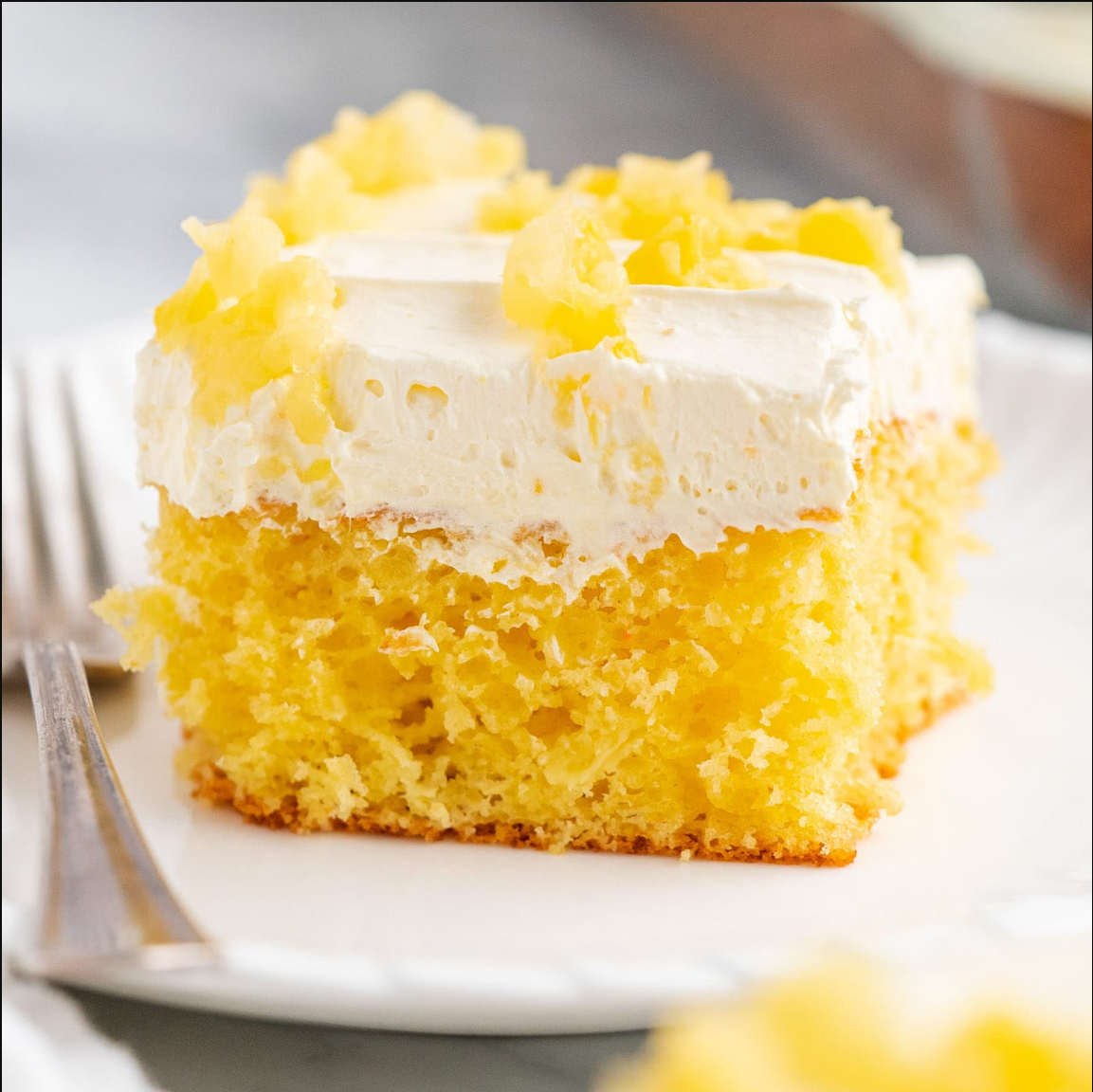 Pineapple Sunshine Cake displayed on a plate, showcasing its golden-yellow hue and creamy topping.