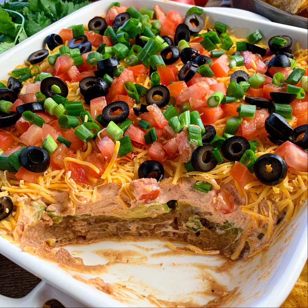 A visual delight with layers of refried beans, sour cream, salsa, cheddar cheese, tomatoes, lettuce, and toppings. Perfect with tortilla chips.